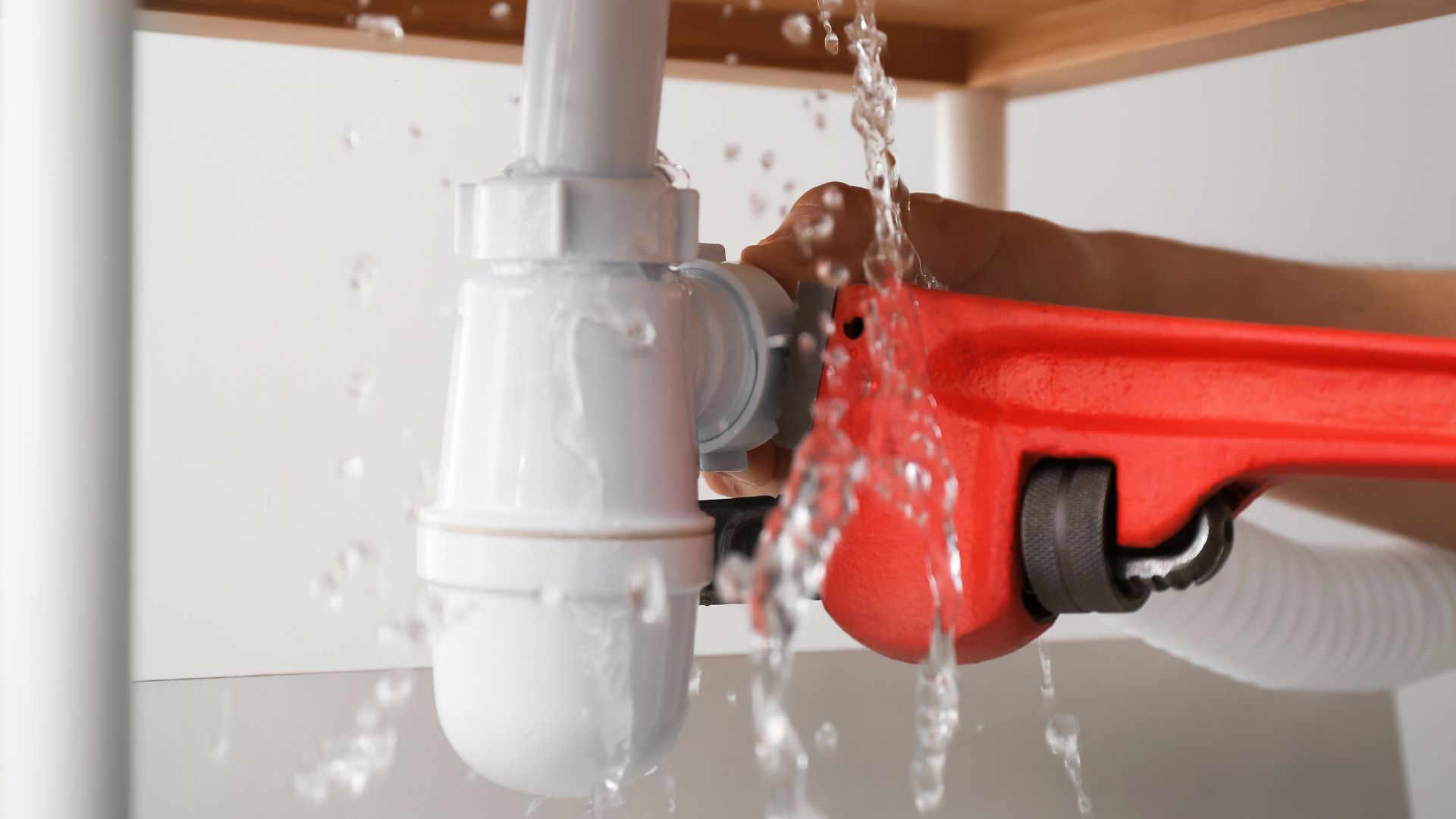 A person holding a red spray gun under a sink